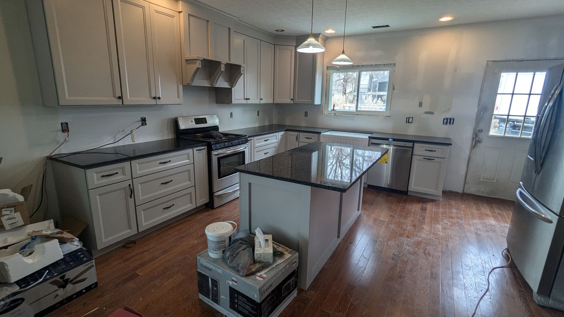A bright, modern kitchen featuring white shaker cabinets, dark granite countertops, a center island, and hardwood floors.