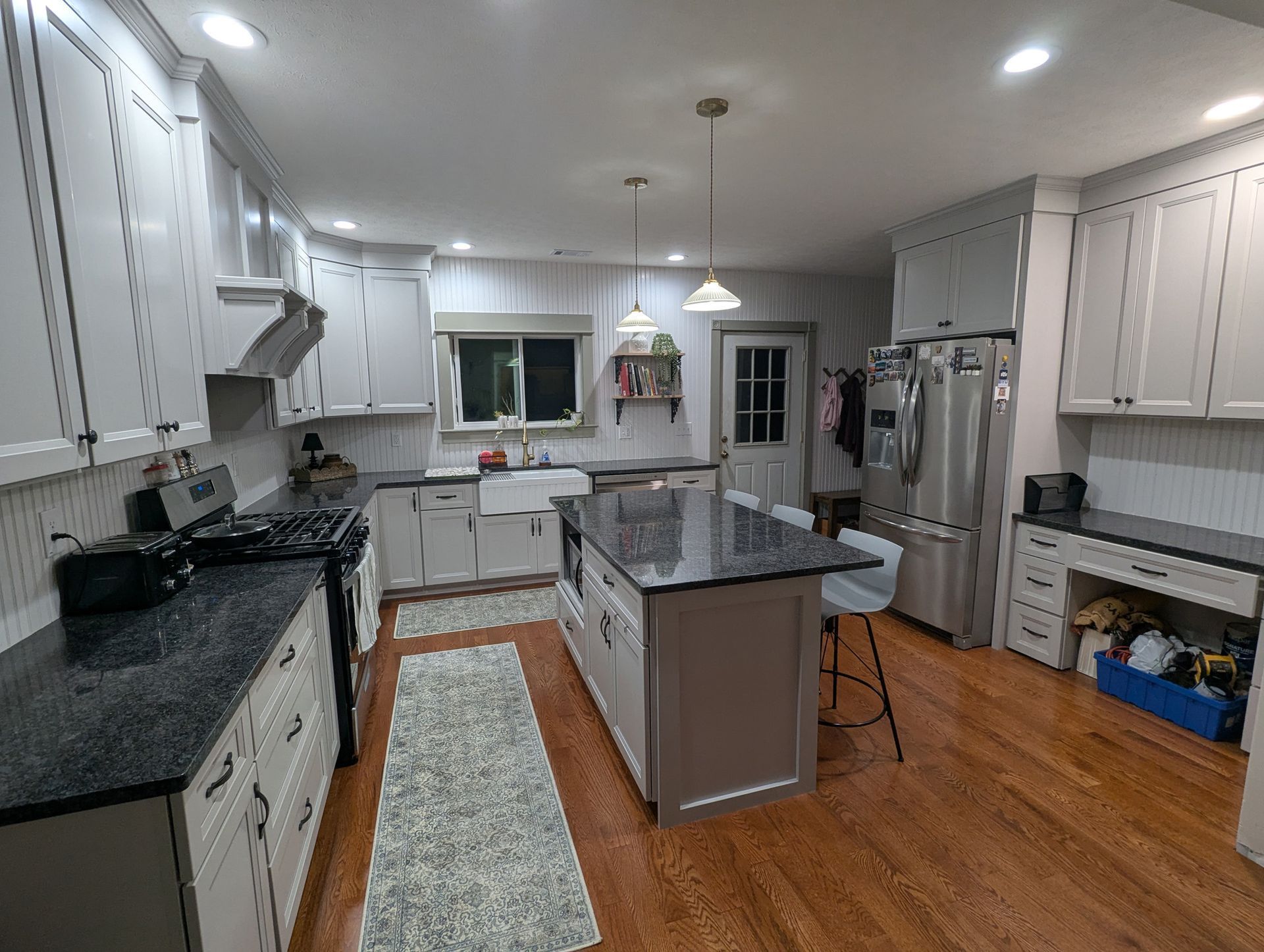 A kitchen featuring white cabinets, a dark granite island, stainless steel appliances, and wood floors.