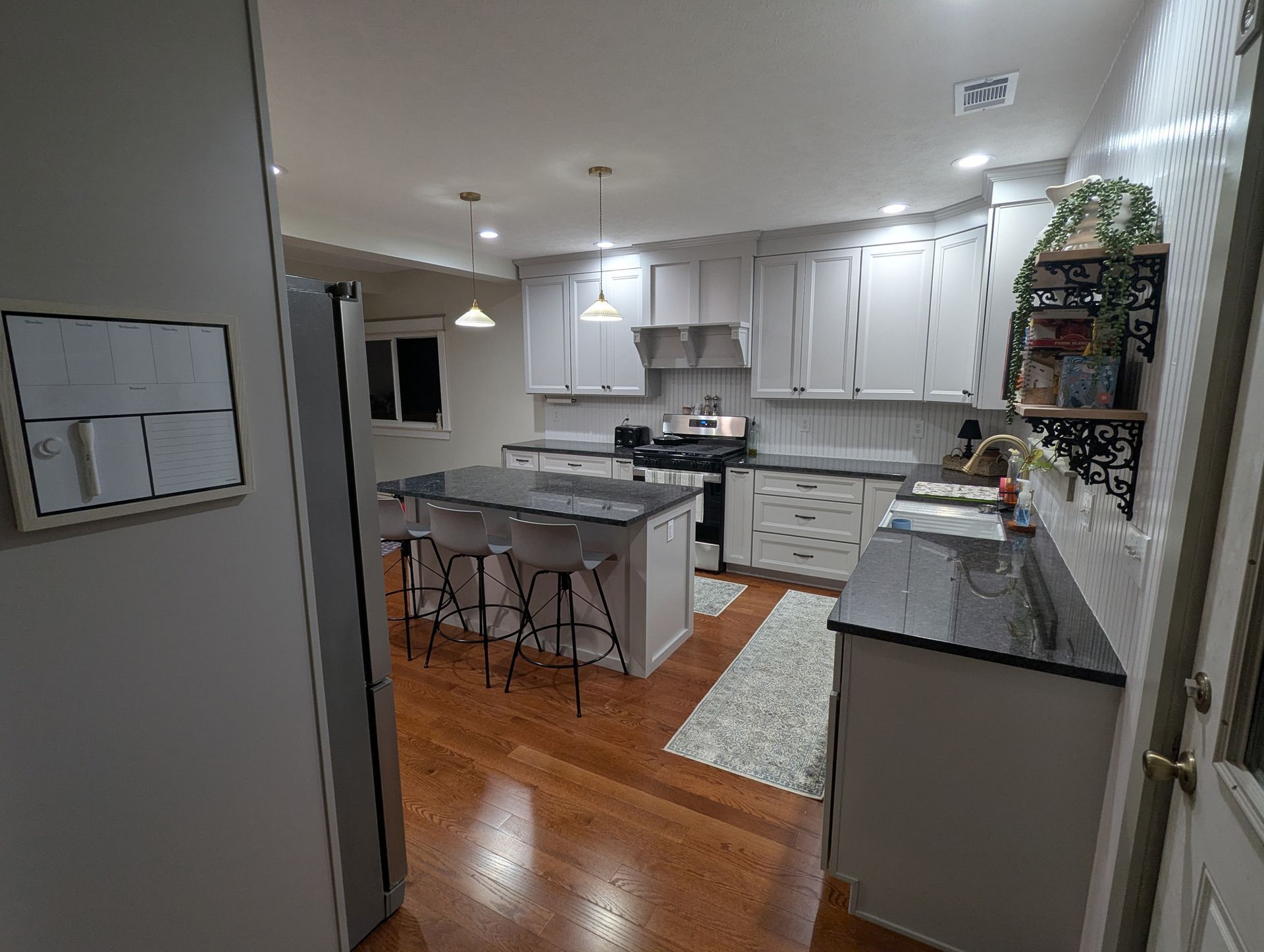 A kitchen with white cabinets, dark countertops, a center island with bar stools, and hardwood floors.