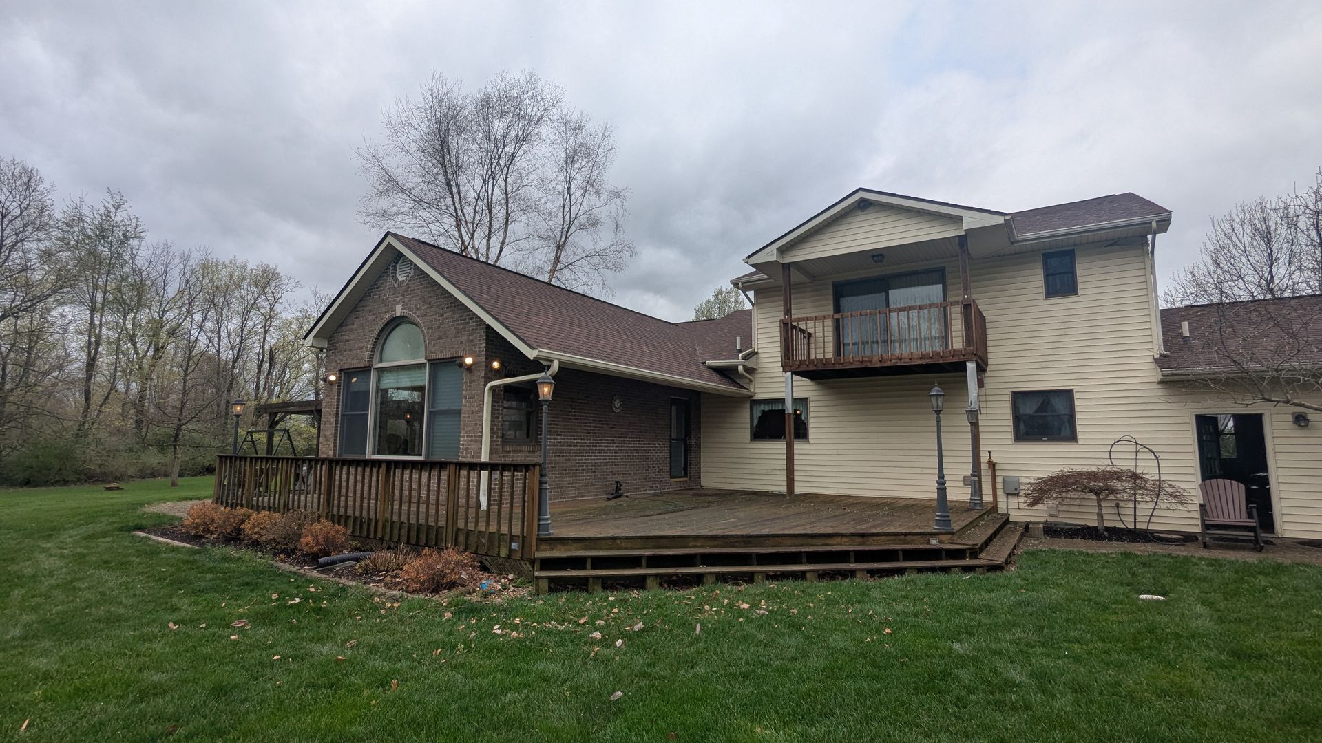 A two-story house with a large wooden deck, brick and cream-colored siding, under a cloudy sky.