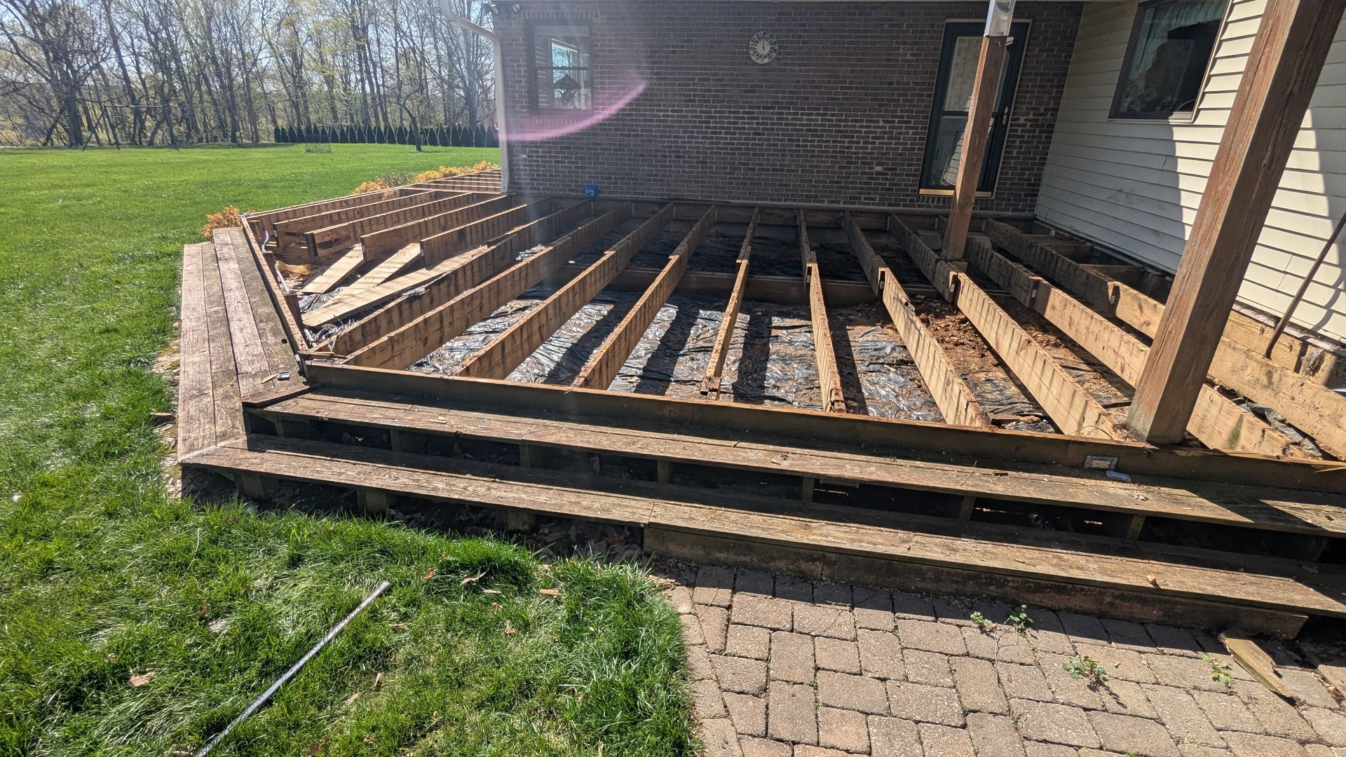 A wooden deck frame under construction outside a home, featuring open joists leading to ground-level steps.
