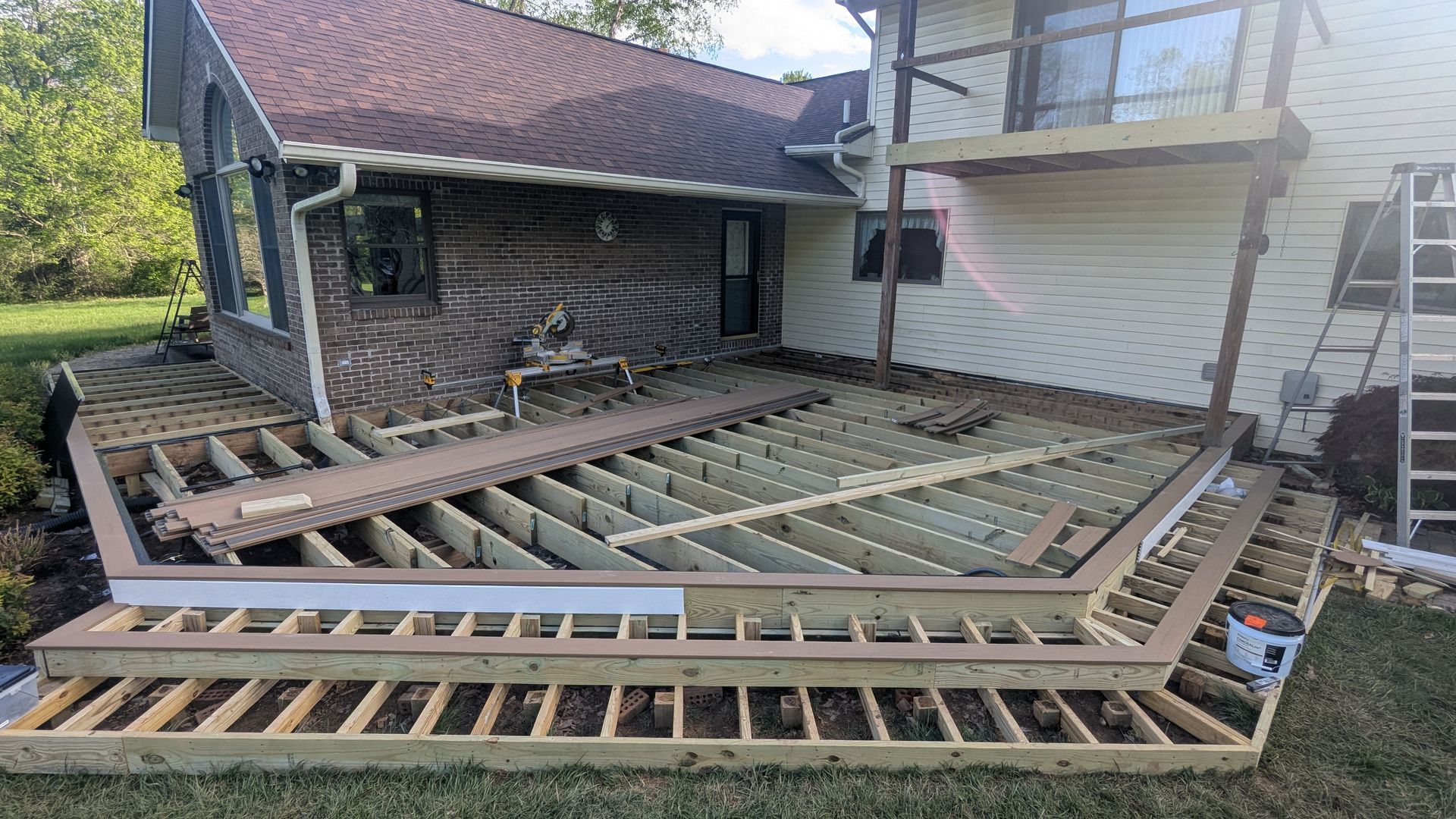 Construction site of a residential deck with wooden framing and partial composite decking installed on a backyard patio.
