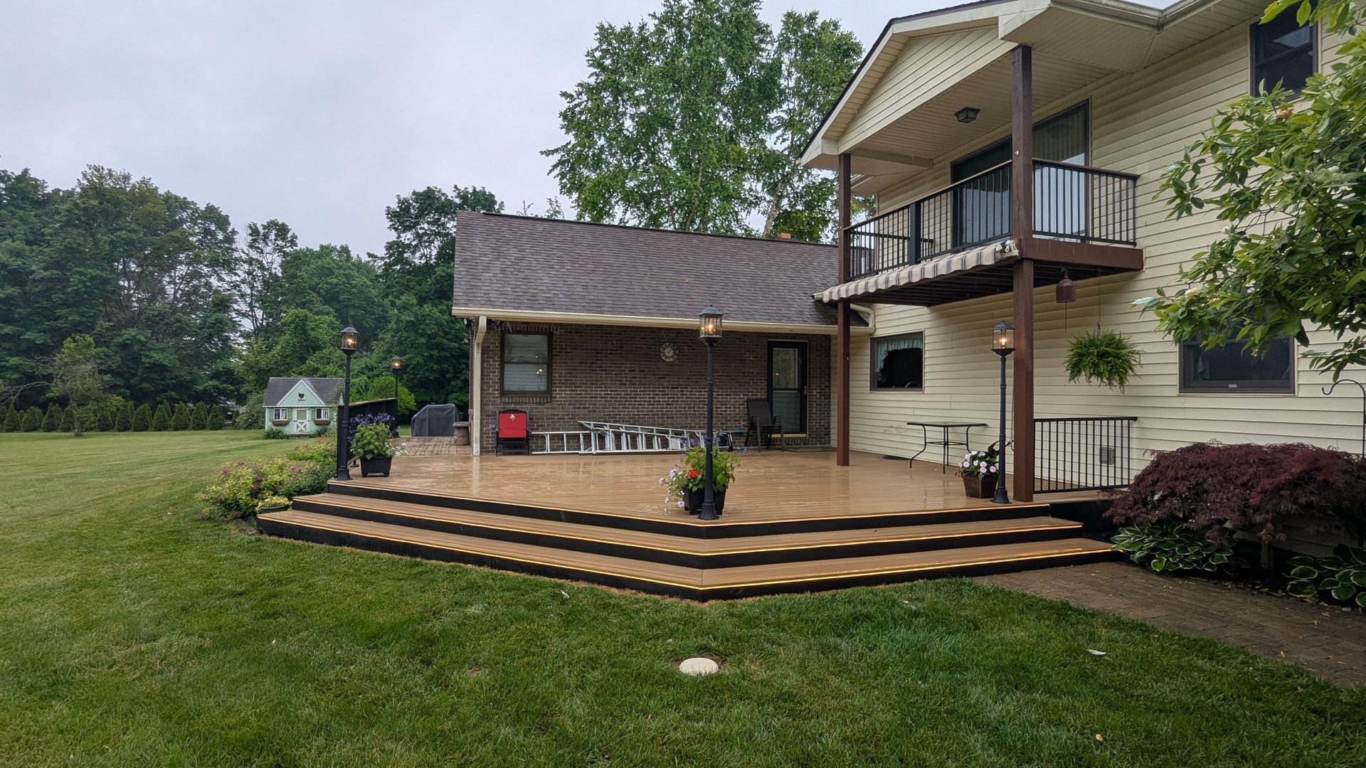 A house exterior featuring a large, multi-level wooden deck transitioning to a lawn, with a balcony above.
