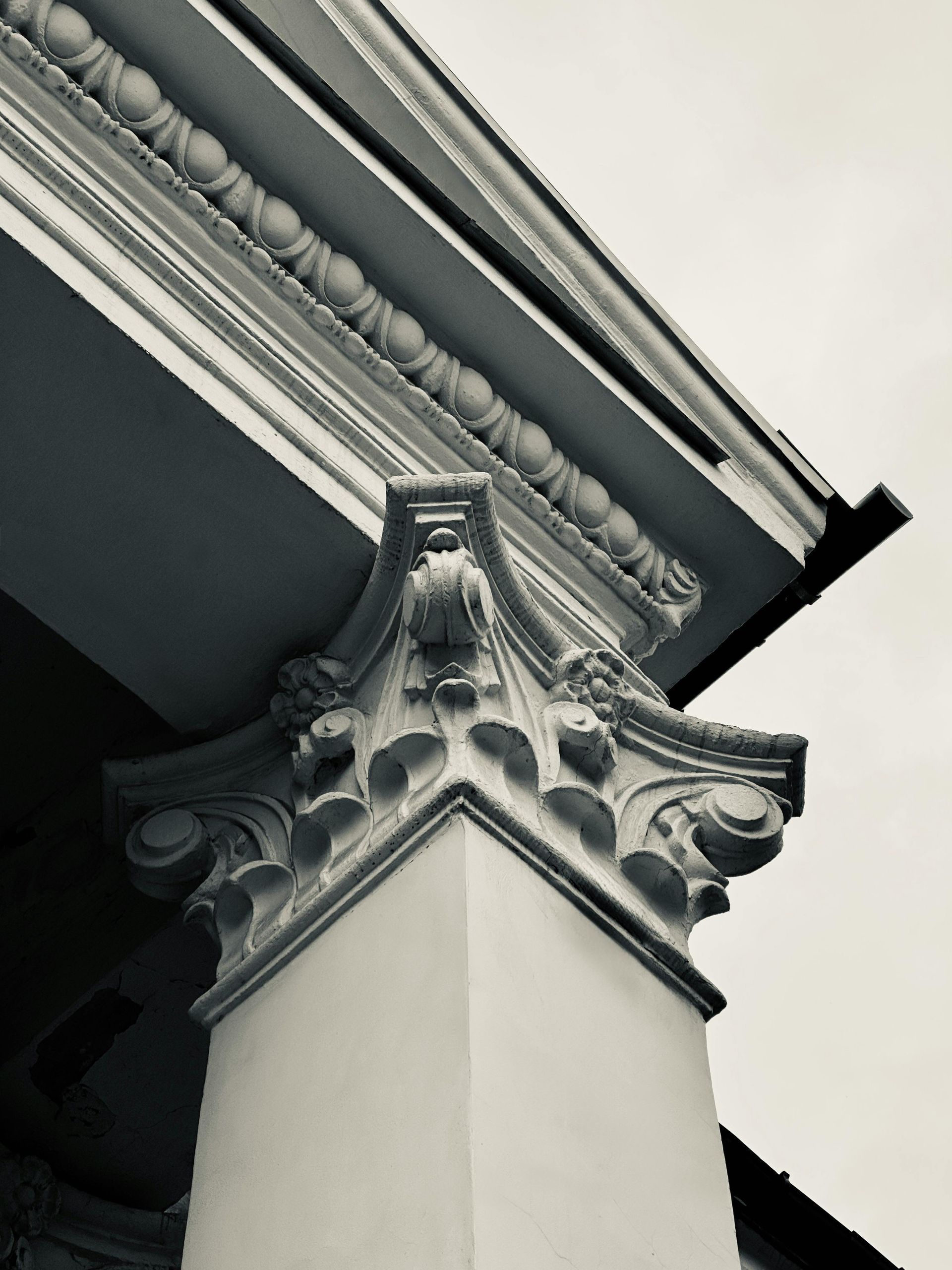 Low-angle view of a white classical building column featuring an ornate capital against a light gray sky.