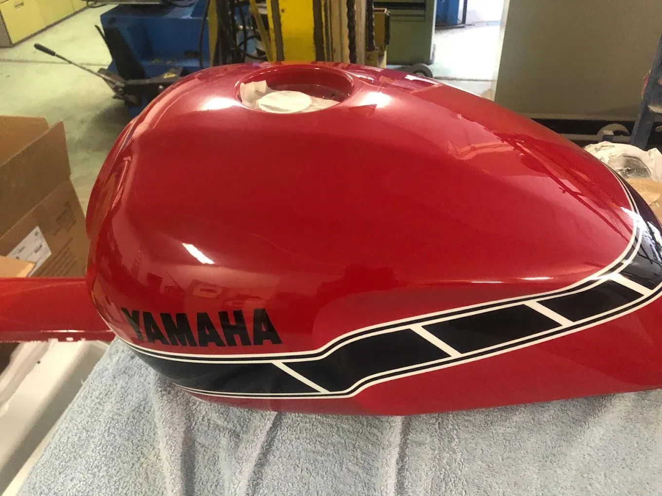 Un réservoir de moto Yamaha rouge est posé sur une serviette bleue