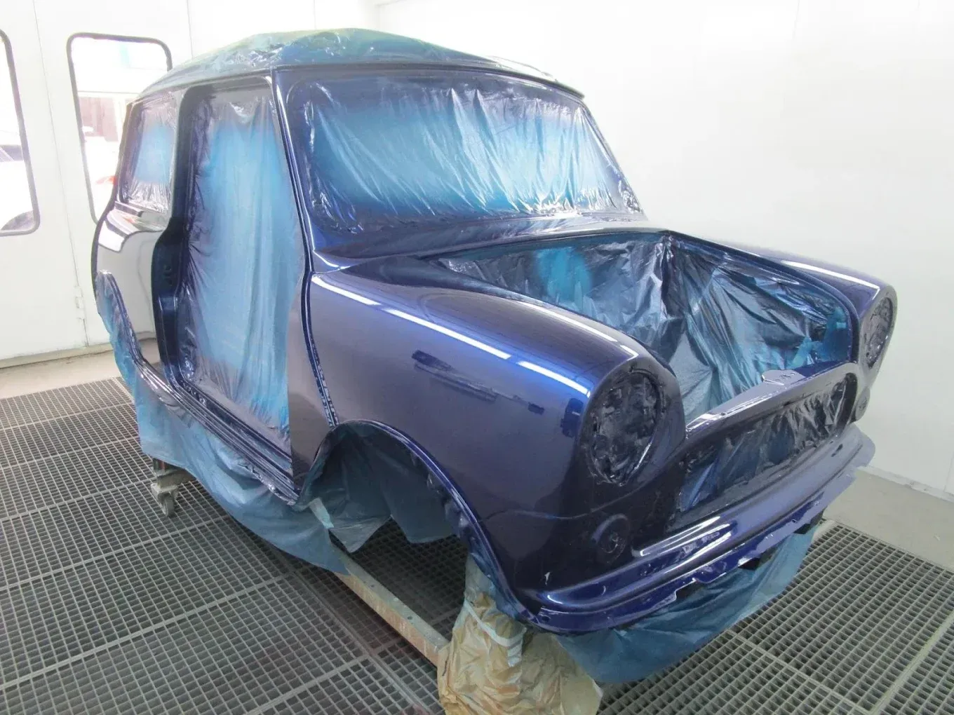 Une voiture bleue est en train d'être peinte dans une cabine de peinture.