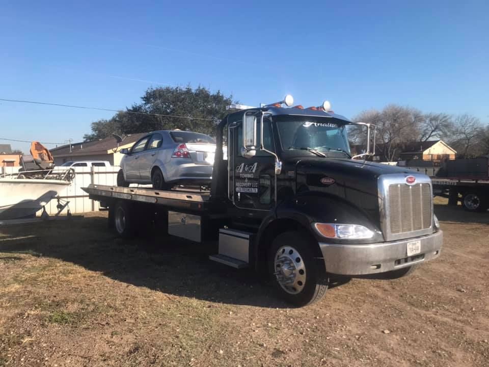 Black tow truck carrying a silver car on a sunny day.