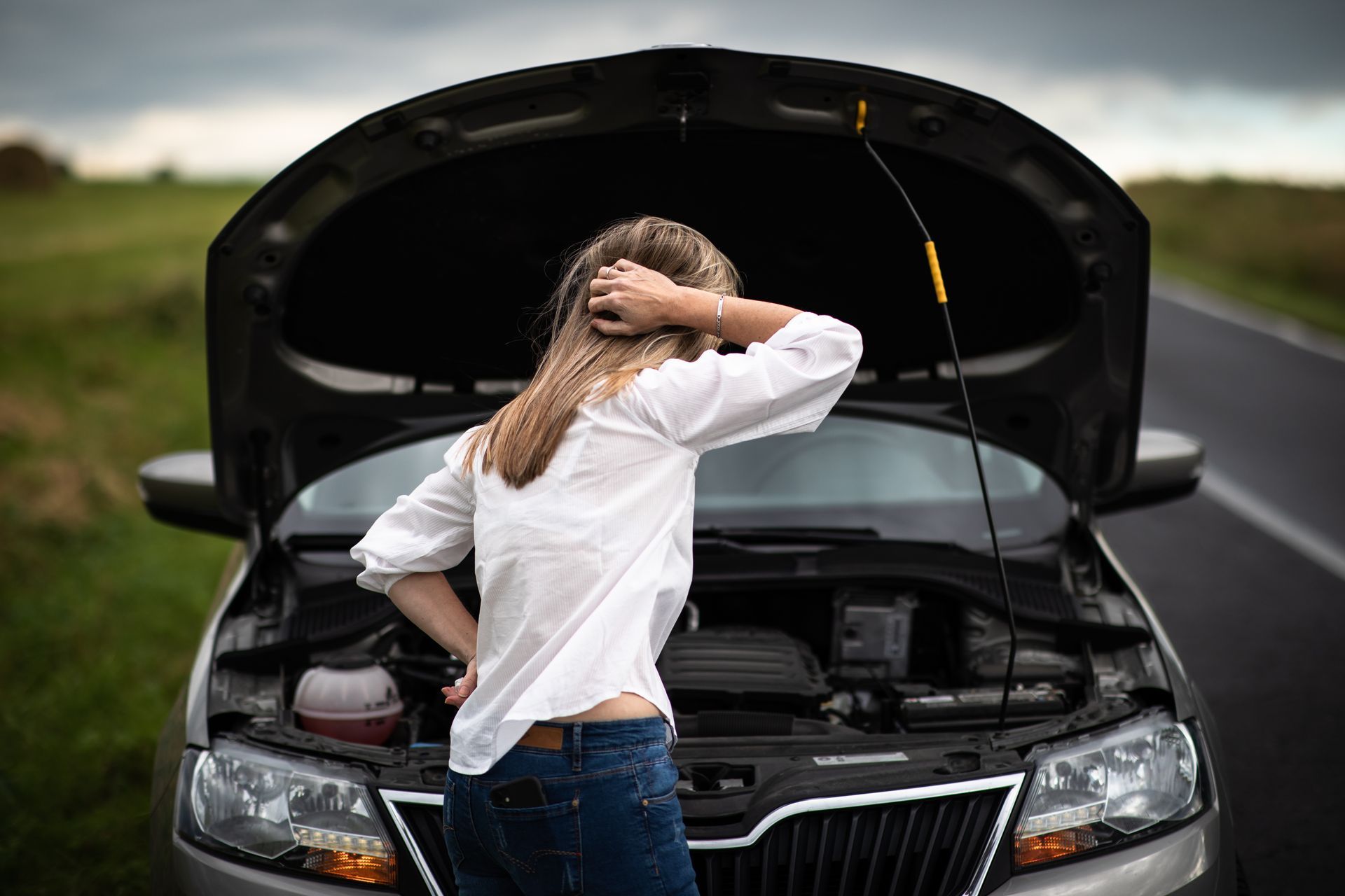 Woman looking at car engine with hood open on roadside.