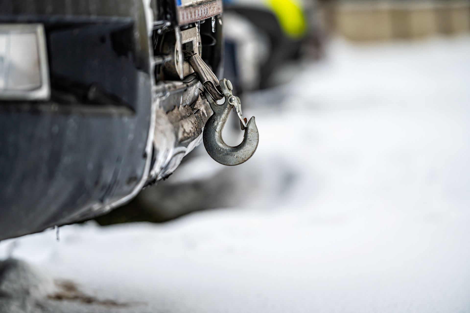 Close-up of a tow hook attached to the back of a black vehicle, with a snowy backdrop.