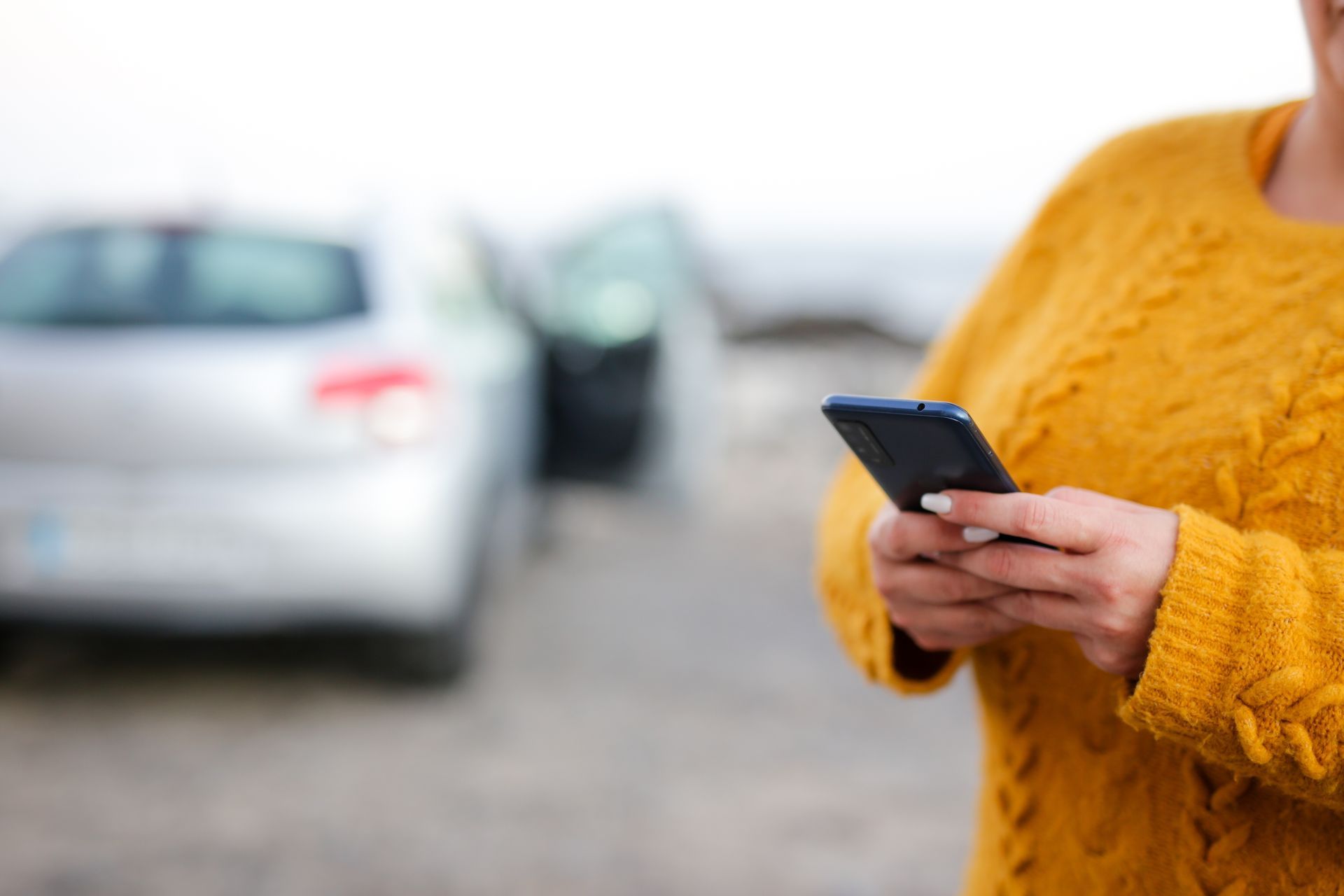 Person in yellow sweater holds a phone in front of a car with an open door.