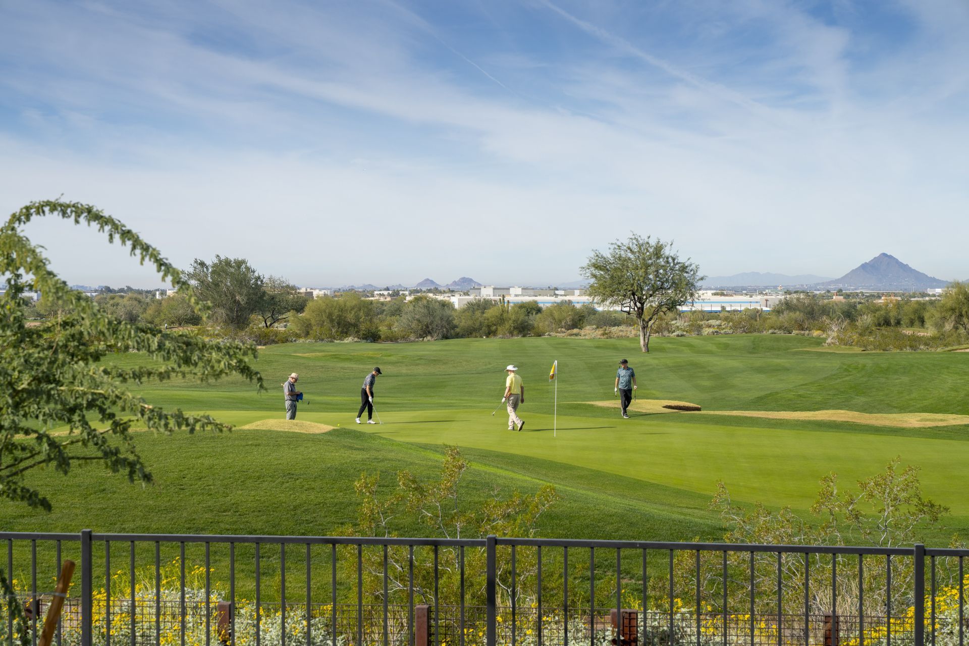 People walking on a green golf course with hills, trees, and a distant mountain under a blue sky.
