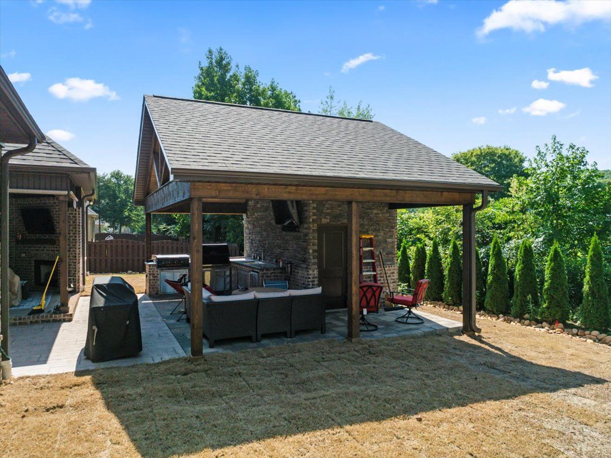 A covered patio area with a grill and a ladder in the backyard of a house.