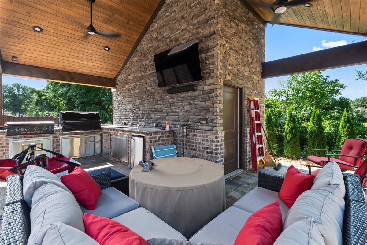 A patio with a couch , table , chairs , and a television.