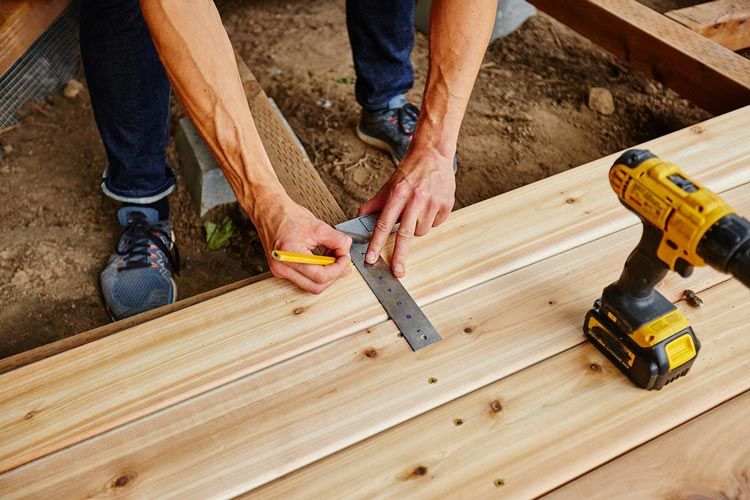 a man is measuring a piece of wood with a ruler next to a drill .