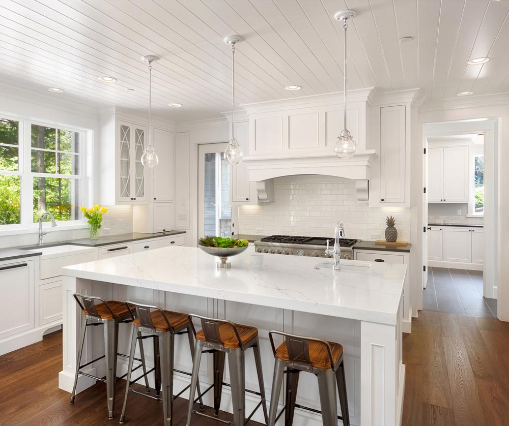 a kitchen with white cabinets , a large island , and stools .