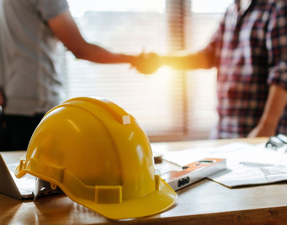 a yellow hard hat is sitting on a wooden table next to two men shaking hands .