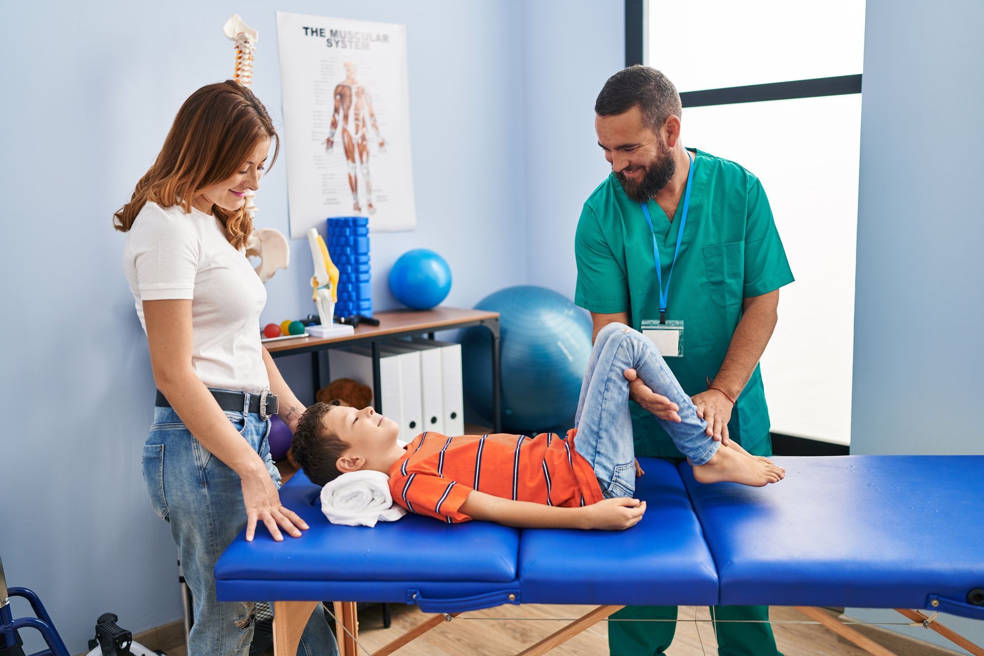 A chiropractor examining a young boy's leg on a treatment table while his mother supports him A chiropractor examining a young boy's leg on a treatment table while his mother supports him