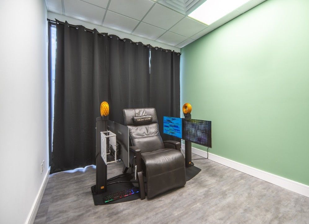 Small therapy room with a reclining chair, monitors, and curtains against green walls.