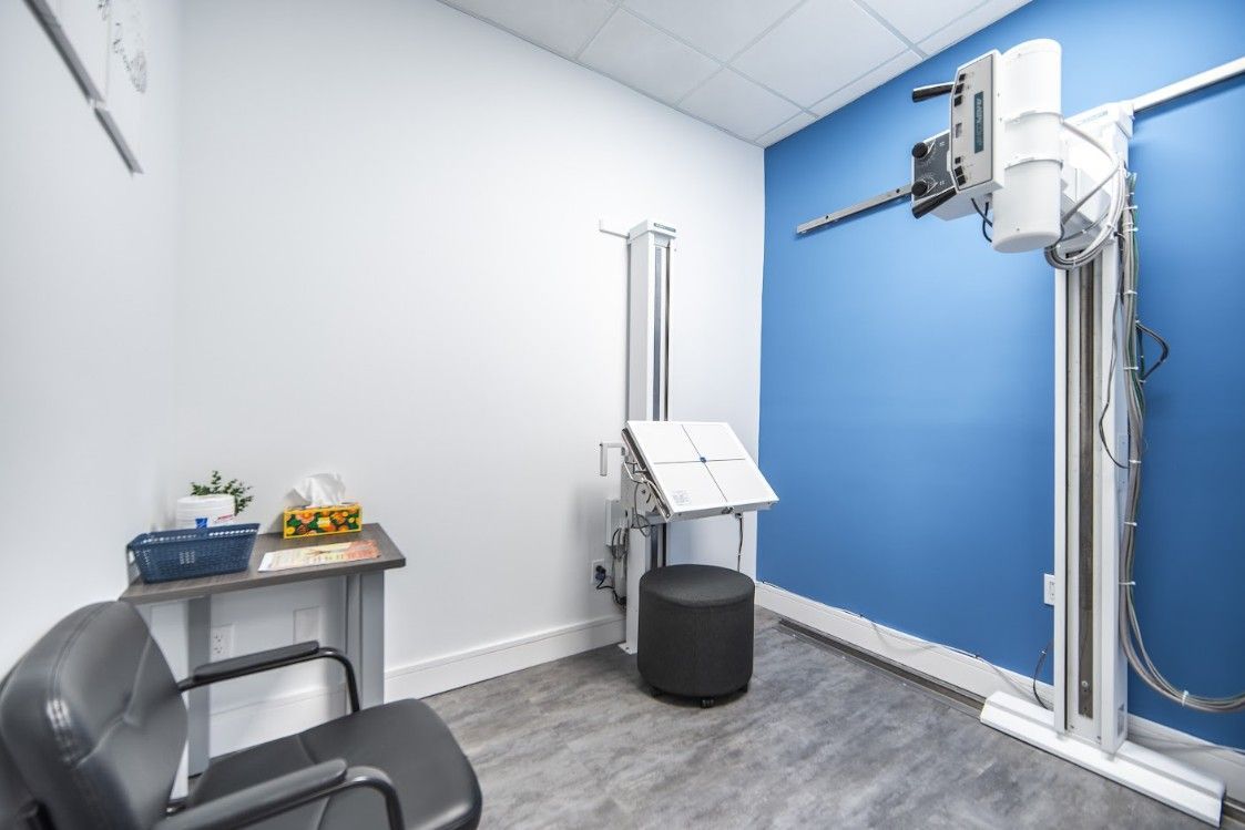 Medical imaging room with x-ray machine, chair, and examination table against blue accent wall