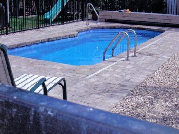 Backyard pool with metal handrail surrounded by stone patio