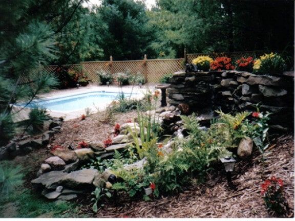 Backyard pool beside a rock waterfall and colorful garden plants