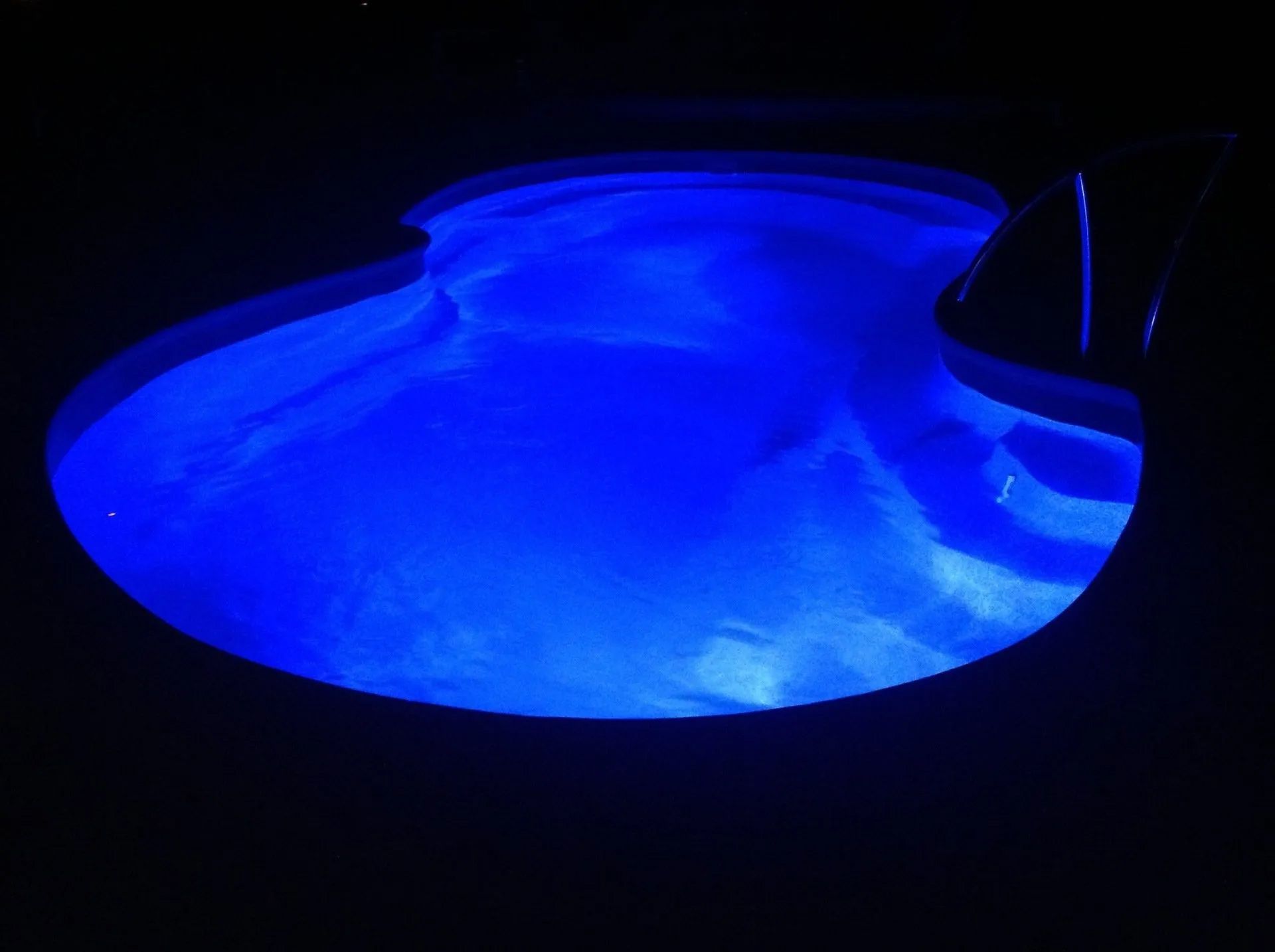 Blue-lit swimming pool at night with glowing water