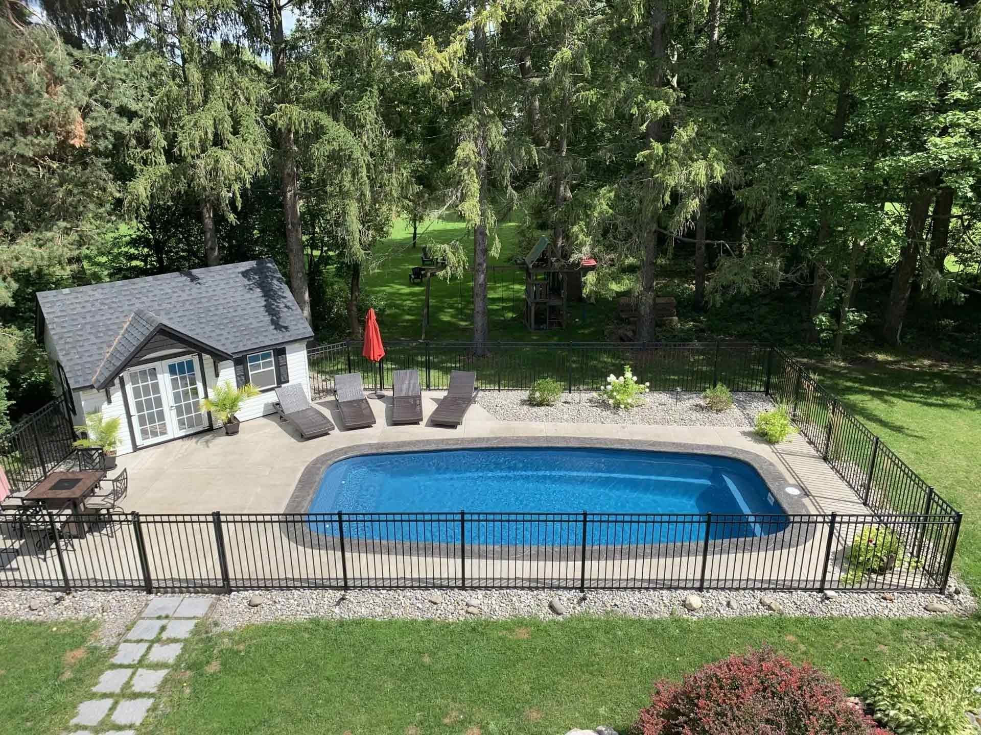 Outdoor pool with stone patio and black fence