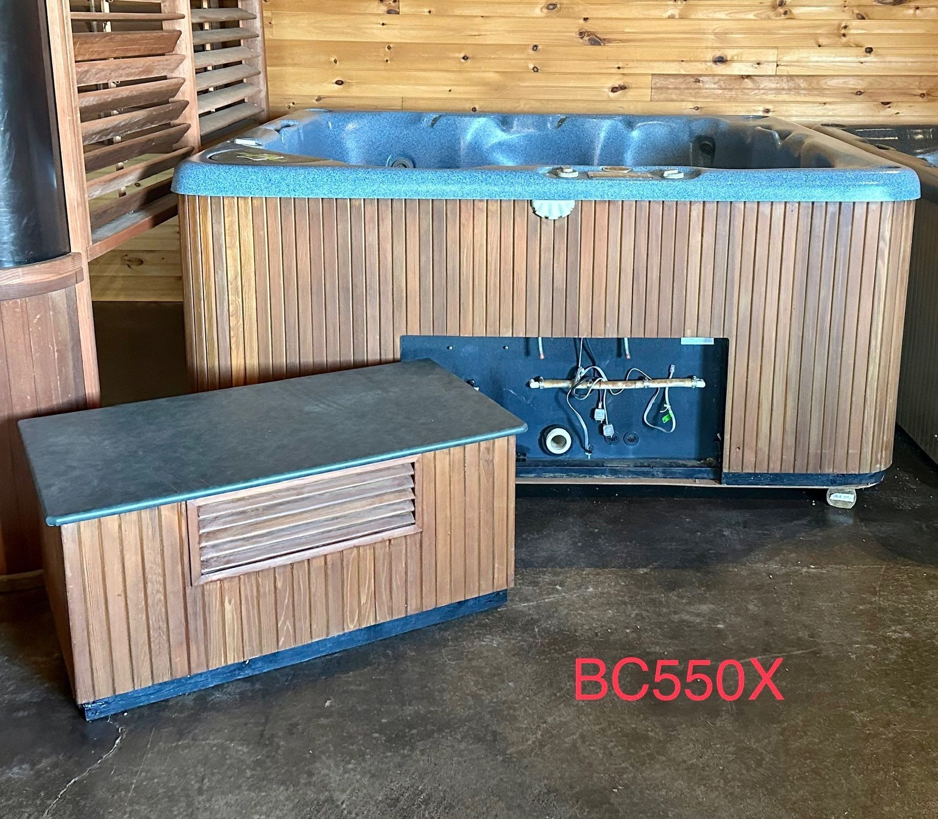 Wood-paneled outdoor hot tub with blue cover and matching storage cabinet on a concrete floor