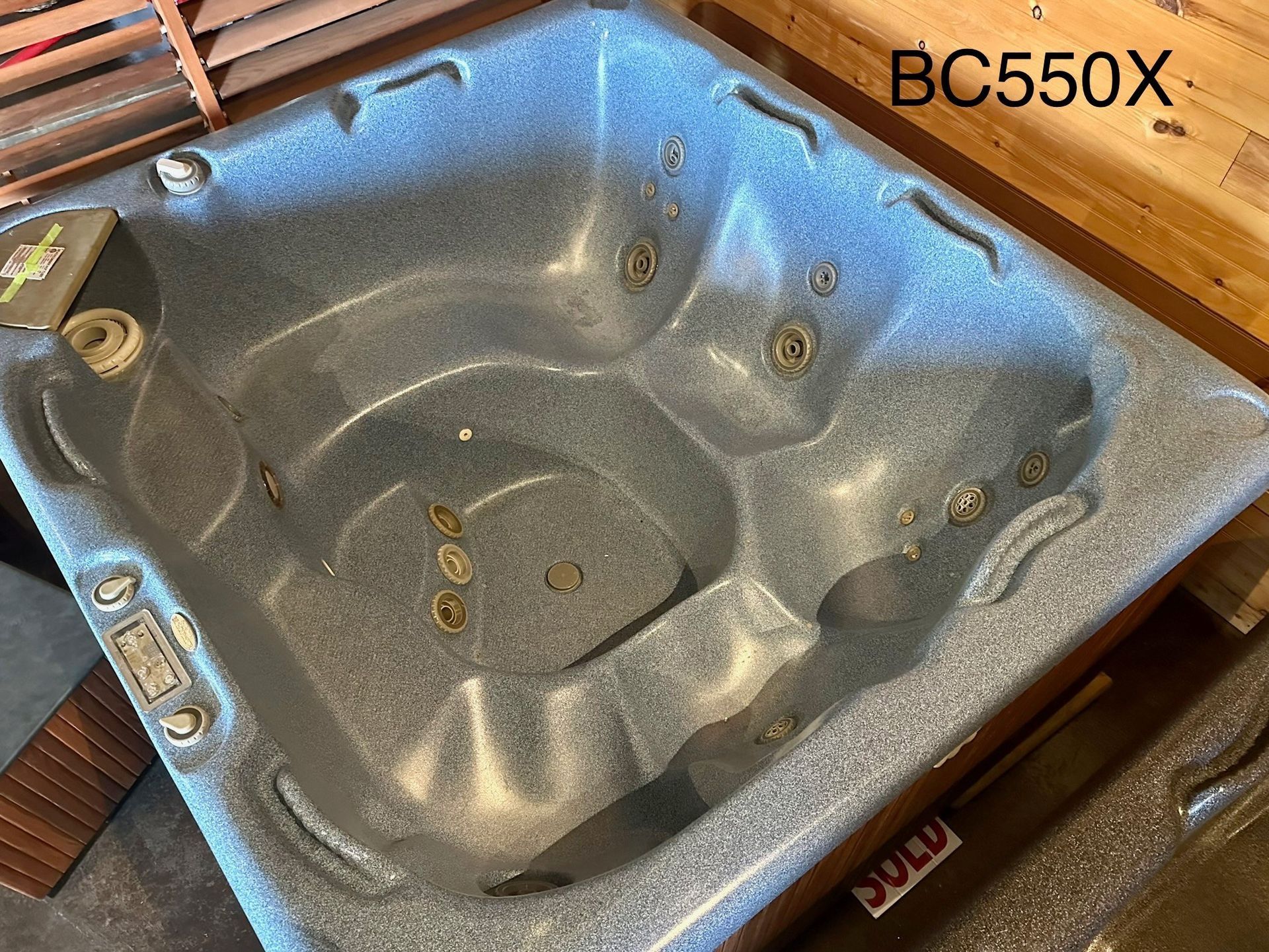 Empty speckled gray hot tub shell with built-in seats and jet holes, labeled “BC550X”