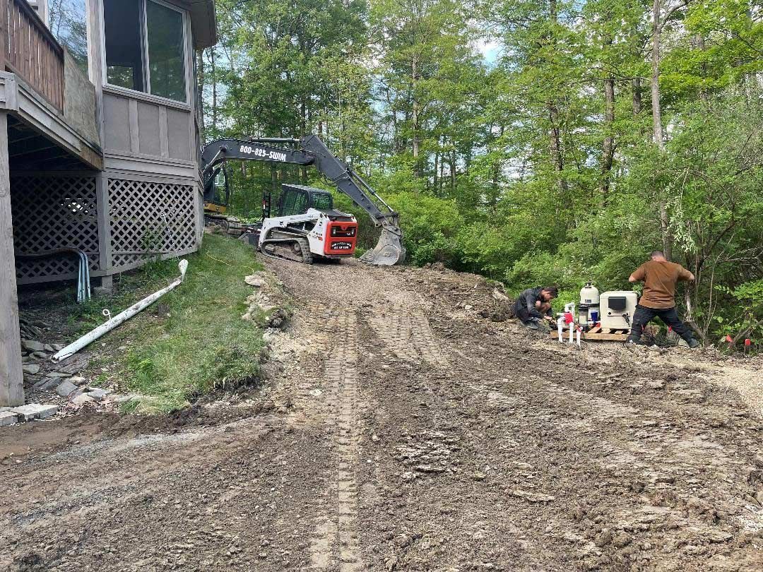 Mini excavator clearing a muddy dirt path beside a house
