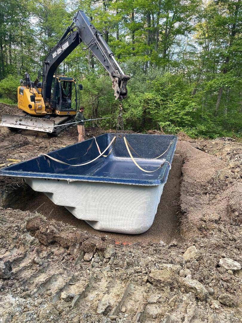 Excavator lifting a large pool container in muddy backyard