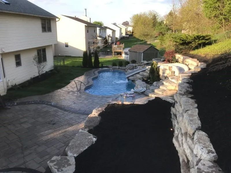 Backyard pool with stone retaining wall beside house