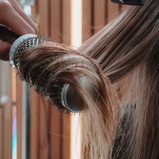Una mujer se seca el cabello con un cepillo redondo.