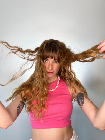 Una mujer con un top corto de color rosa sostiene su cabello en sus manos.