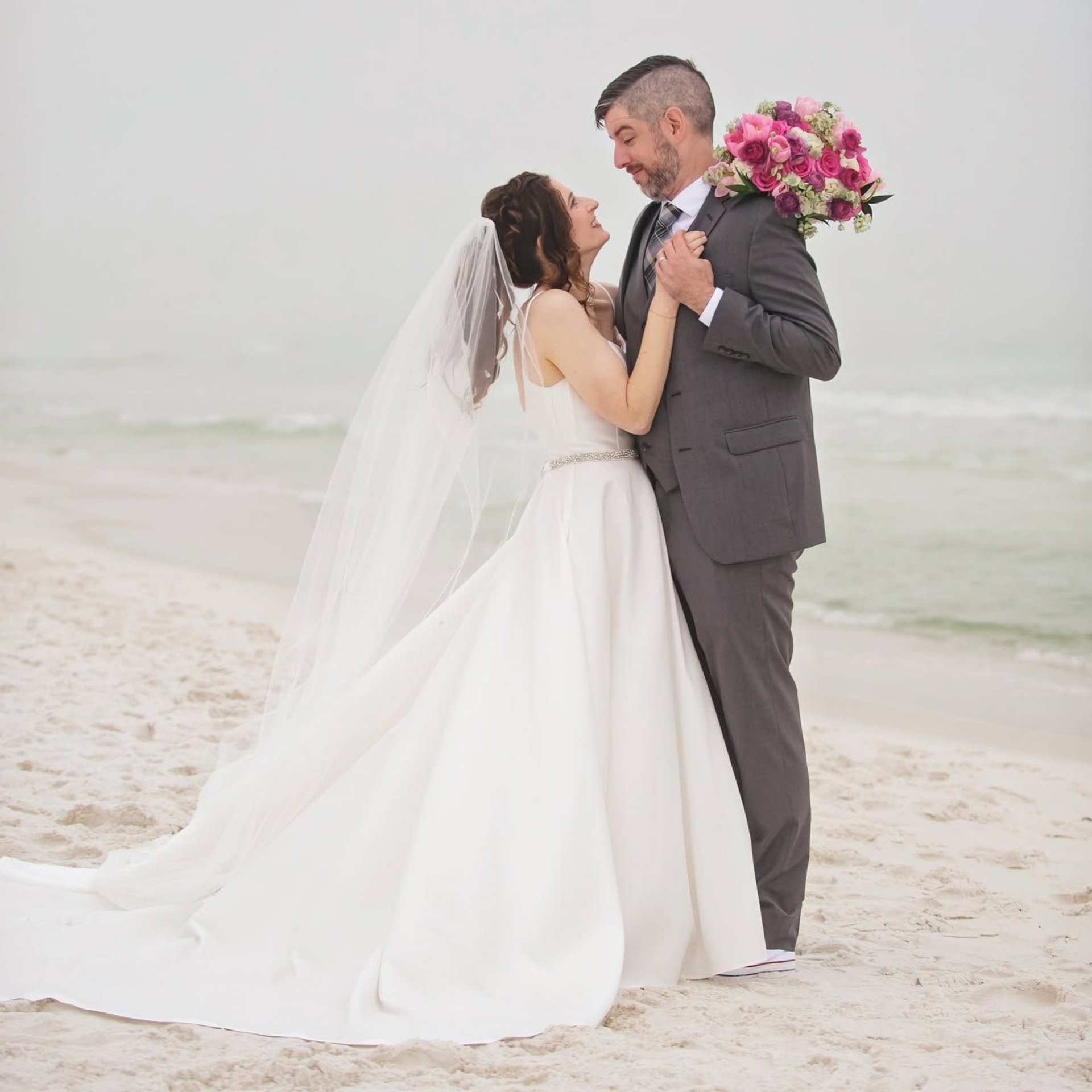Couple exchanging vows at a beach wedding under a floral arch