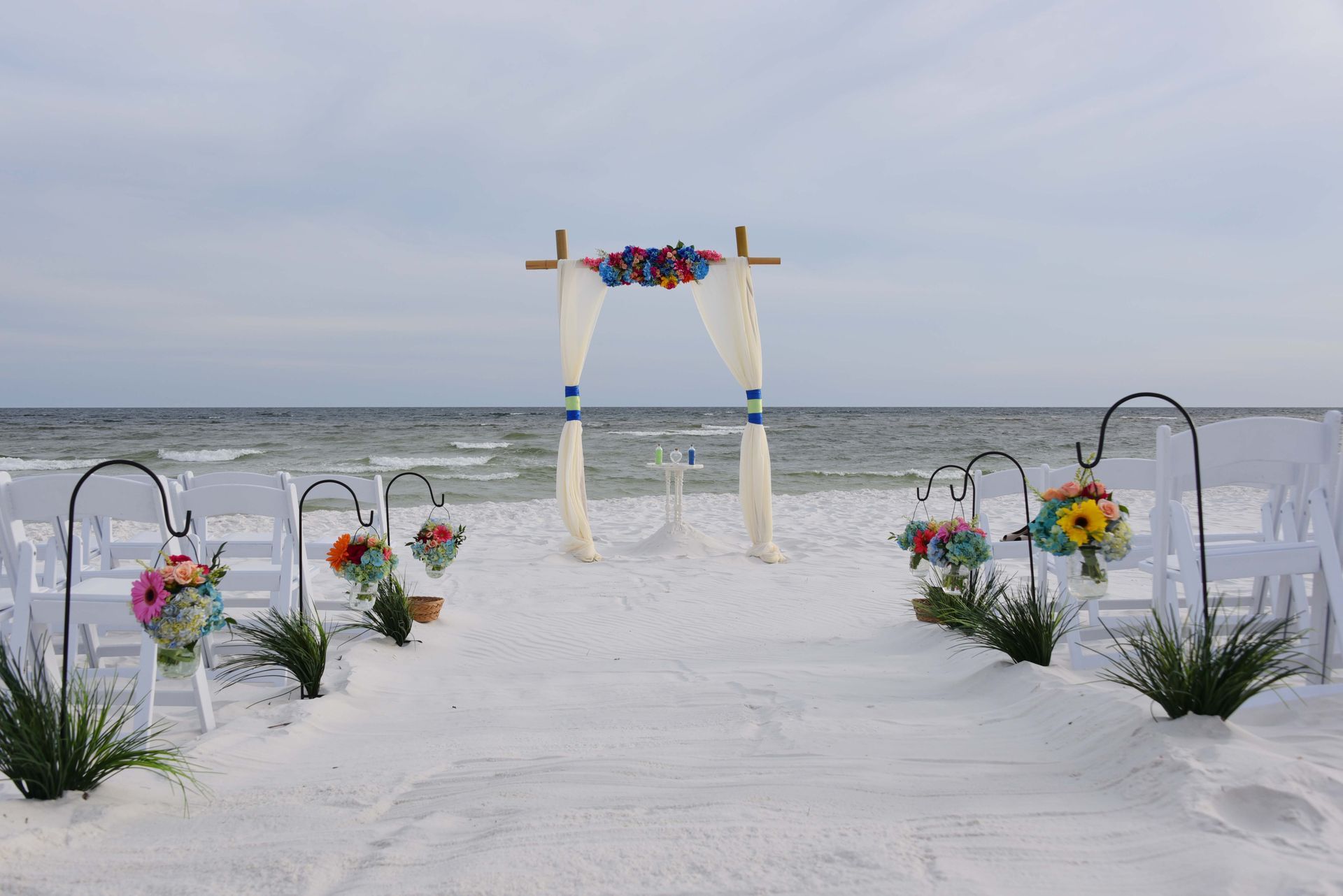 Beach wedding arch decorated with flowers on white sand by the ocean