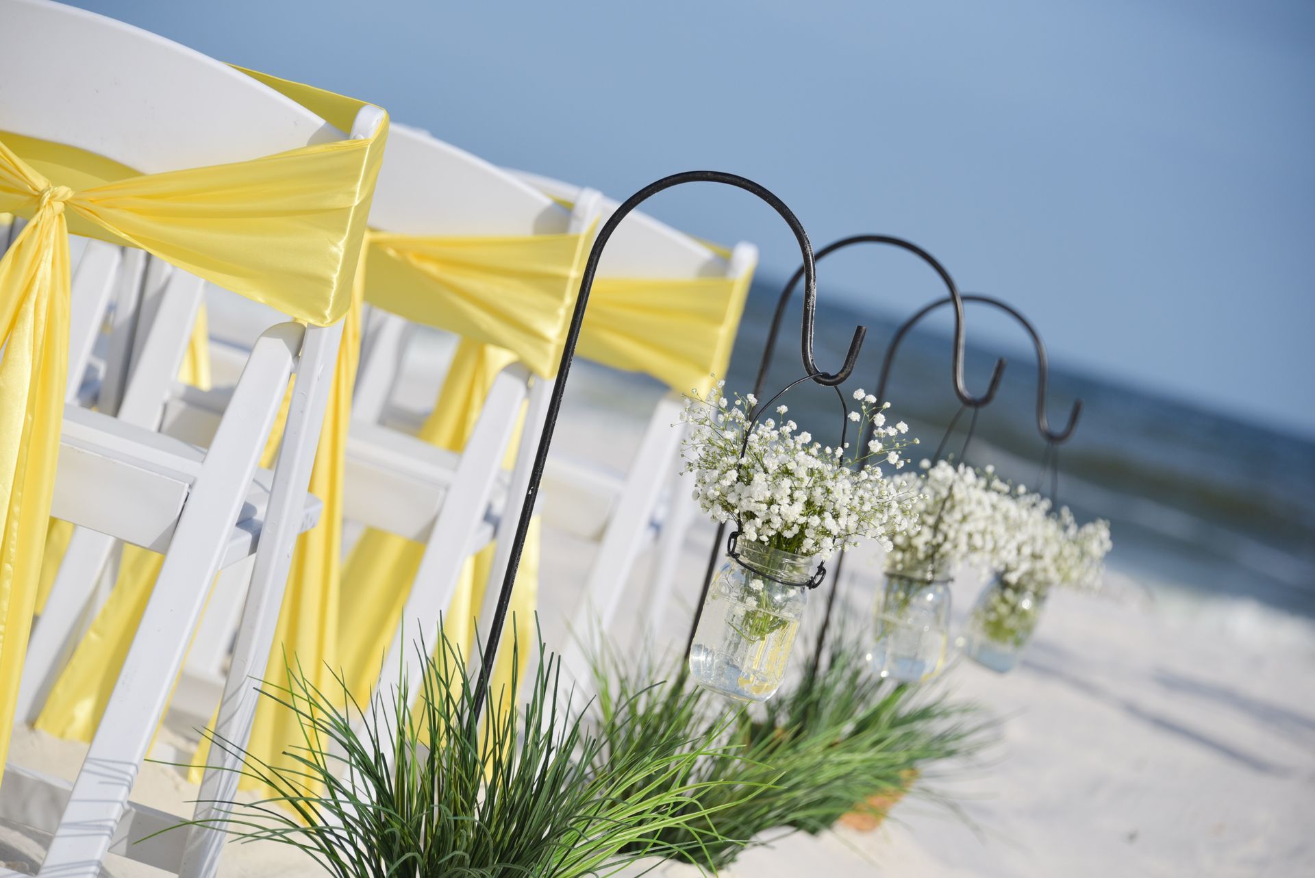 Beach wedding chairs with yellow ribbons and white flowers in the sand