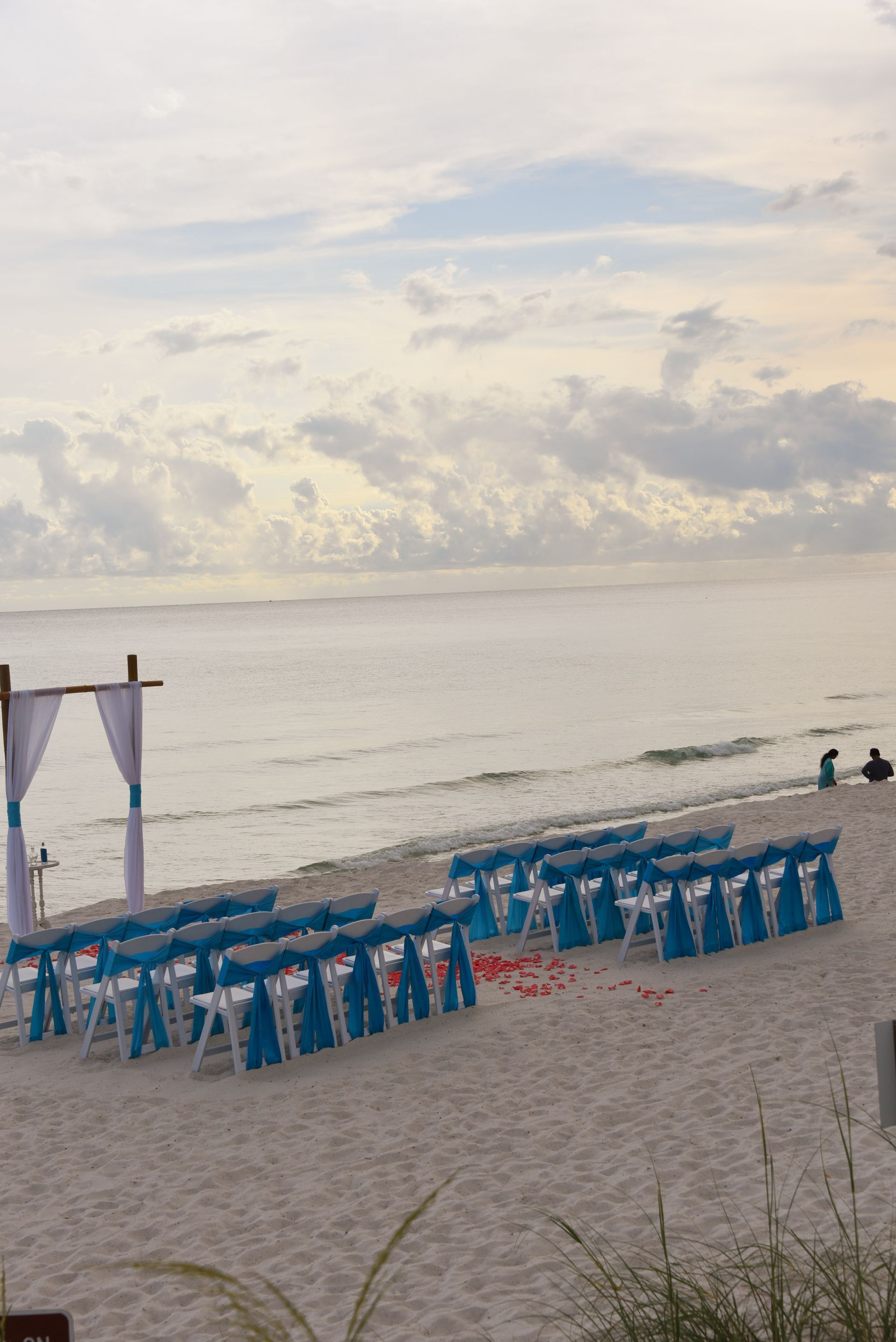 Beach setup with blue chairs and a canopy facing a calm ocean at sunset