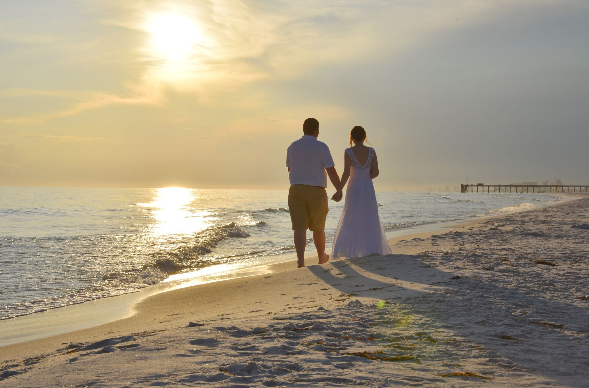 Couple walking hand in hand on a beach at sunset with ocean waves and warm golden light