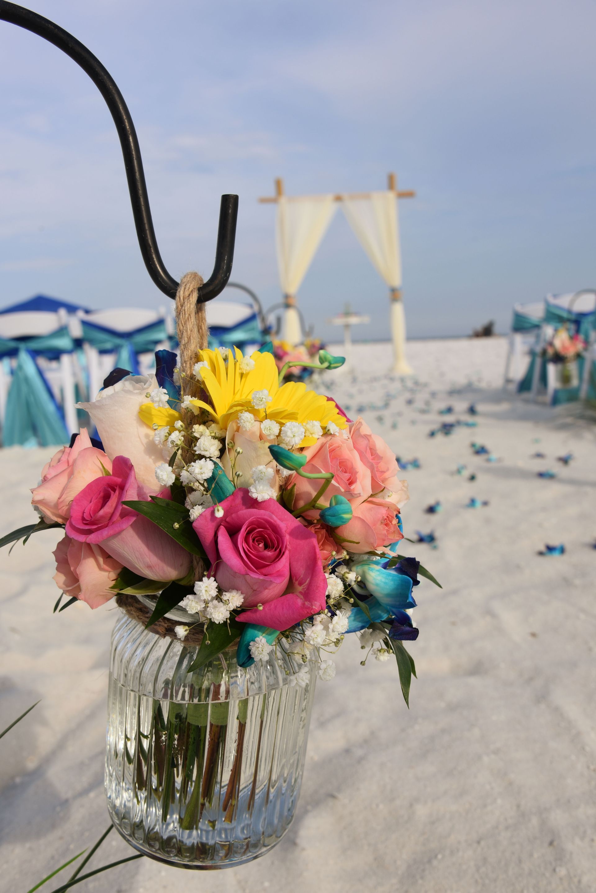 Colorful bouquet in a glass vase on a sandy beach with cabanas in the background