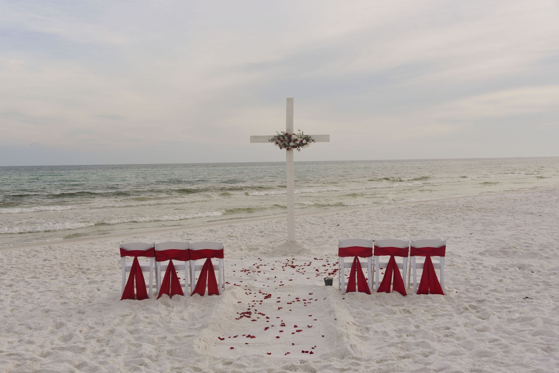 Beach altar with white cross and red ribbons on a snowy shore by the sea