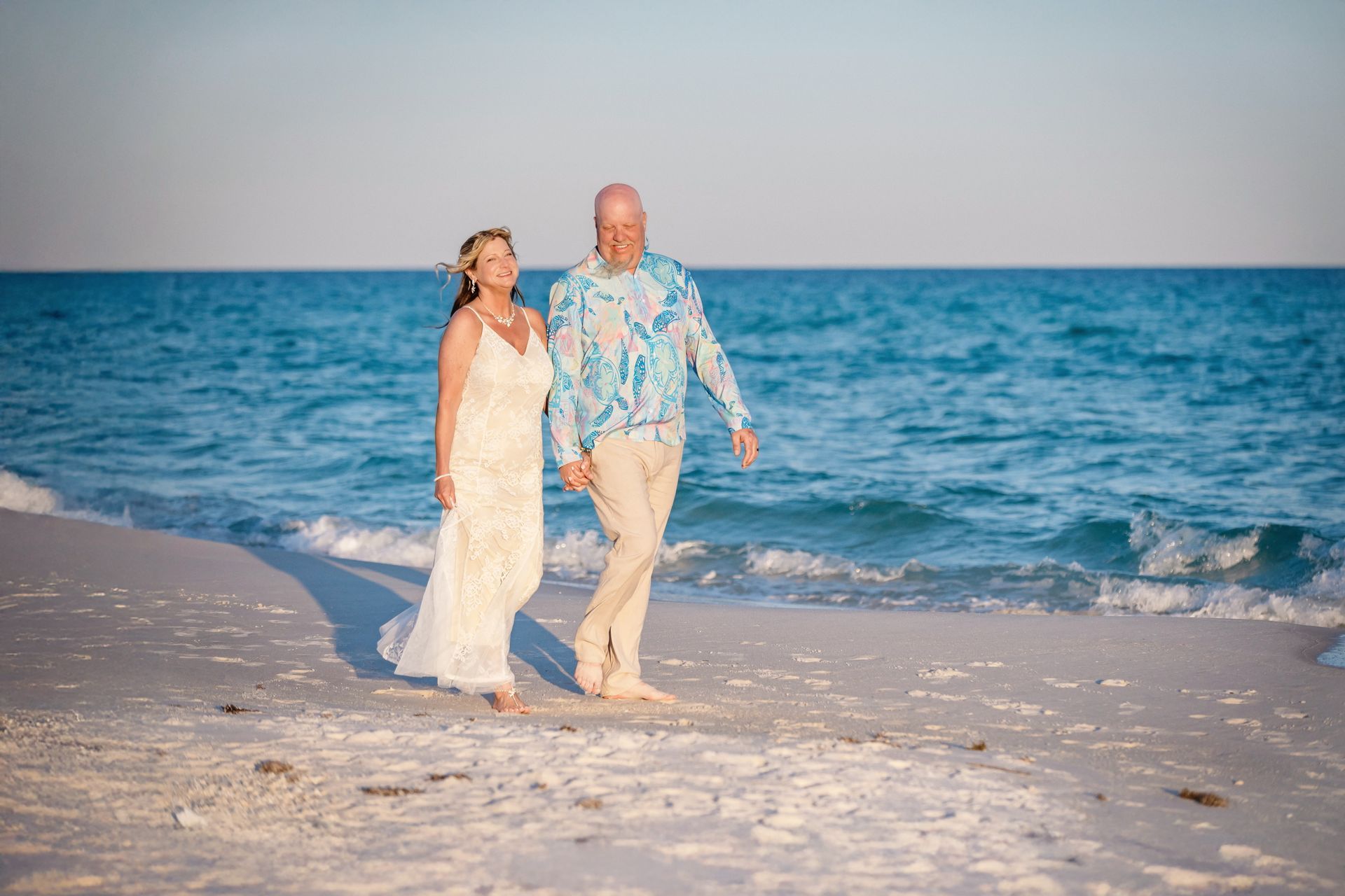 Couple walking hand in hand along a sunny beach beside blue ocean waves