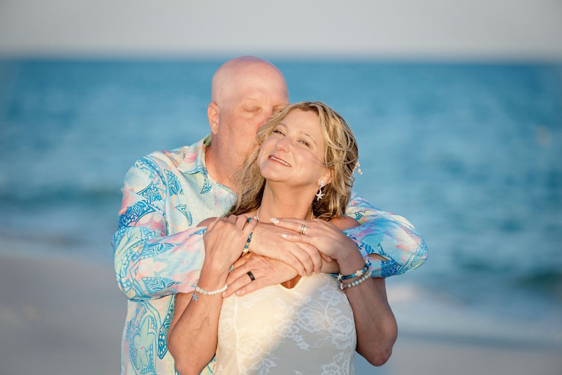 Couple embracing on a beach at sunset, with ocean waves in the background