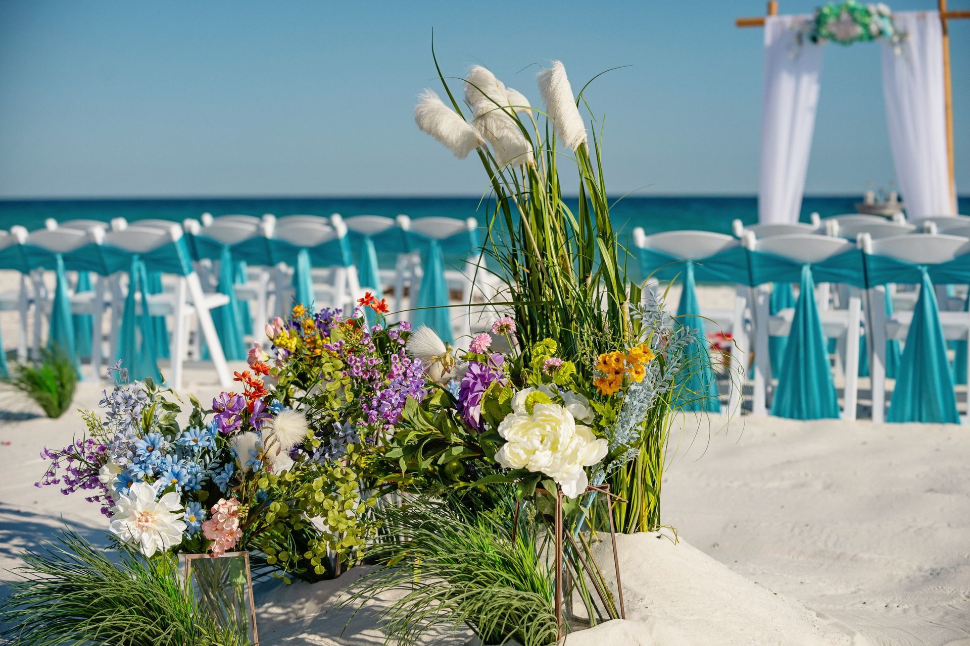 Floral arrangement on a beach wedding setup with turquoise chairs and white umbrellas by the sea