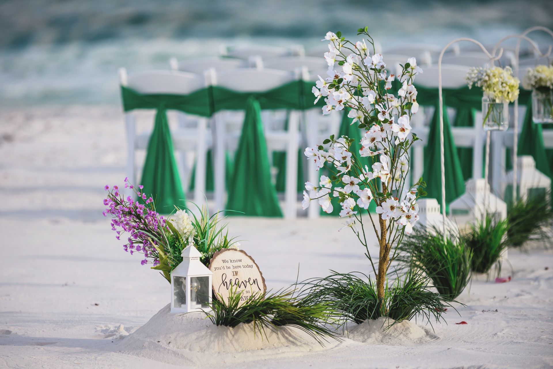 Beach wedding setup with white floral arrangements and green chairs on the sand