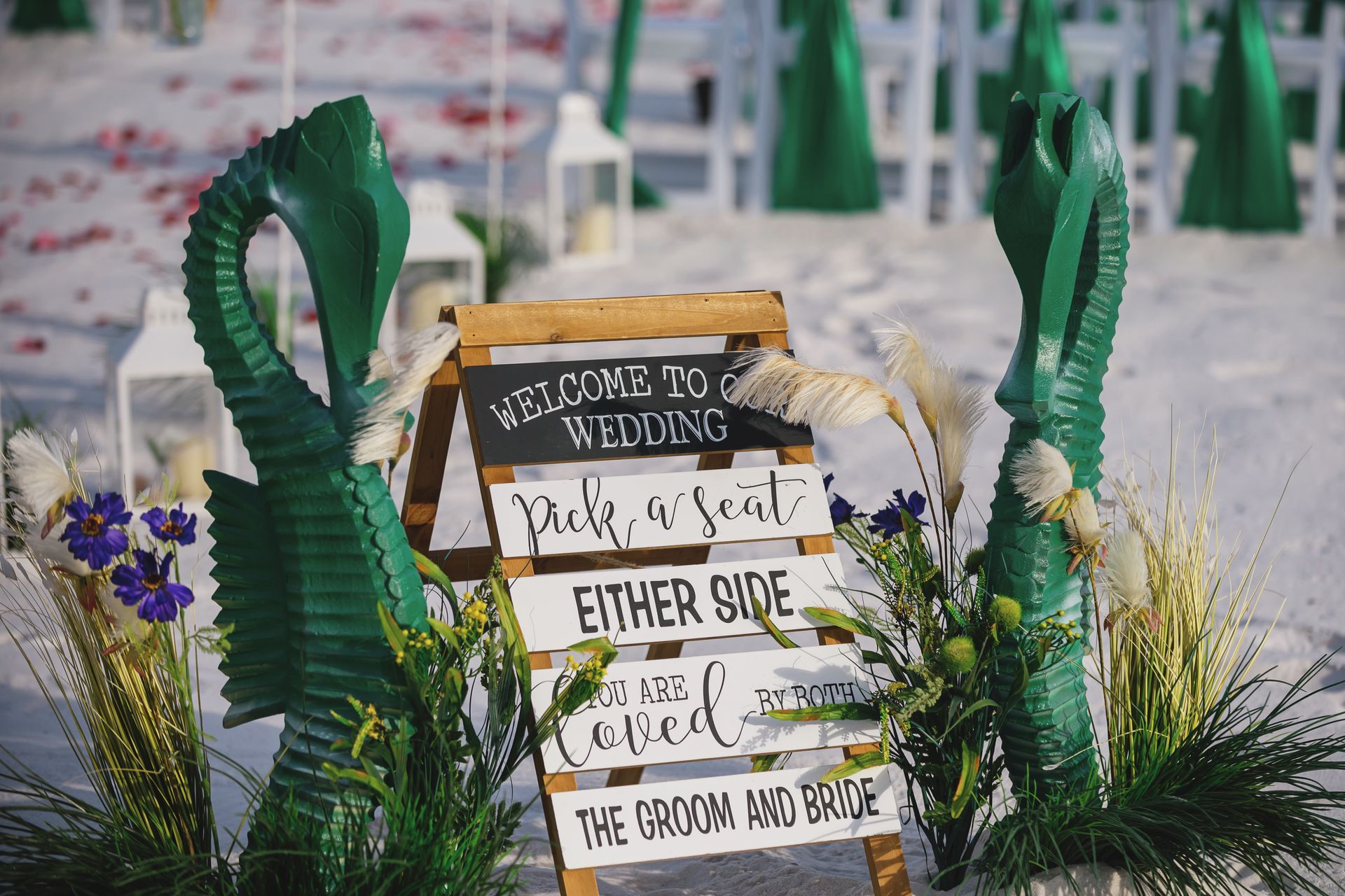 Rustic wedding welcome sign with white and black lettering, greenery, and purple flowers in a garden setting
