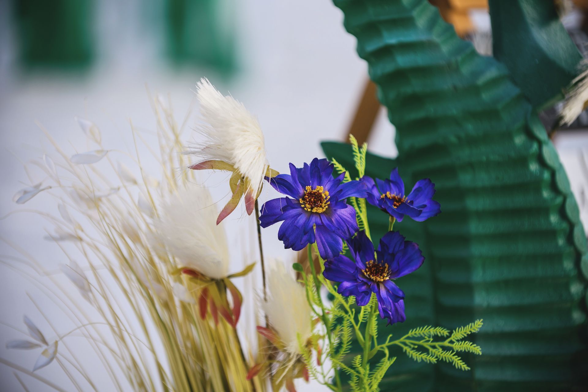 Purple flowers and white dried grasses arranged beside a large green leaf