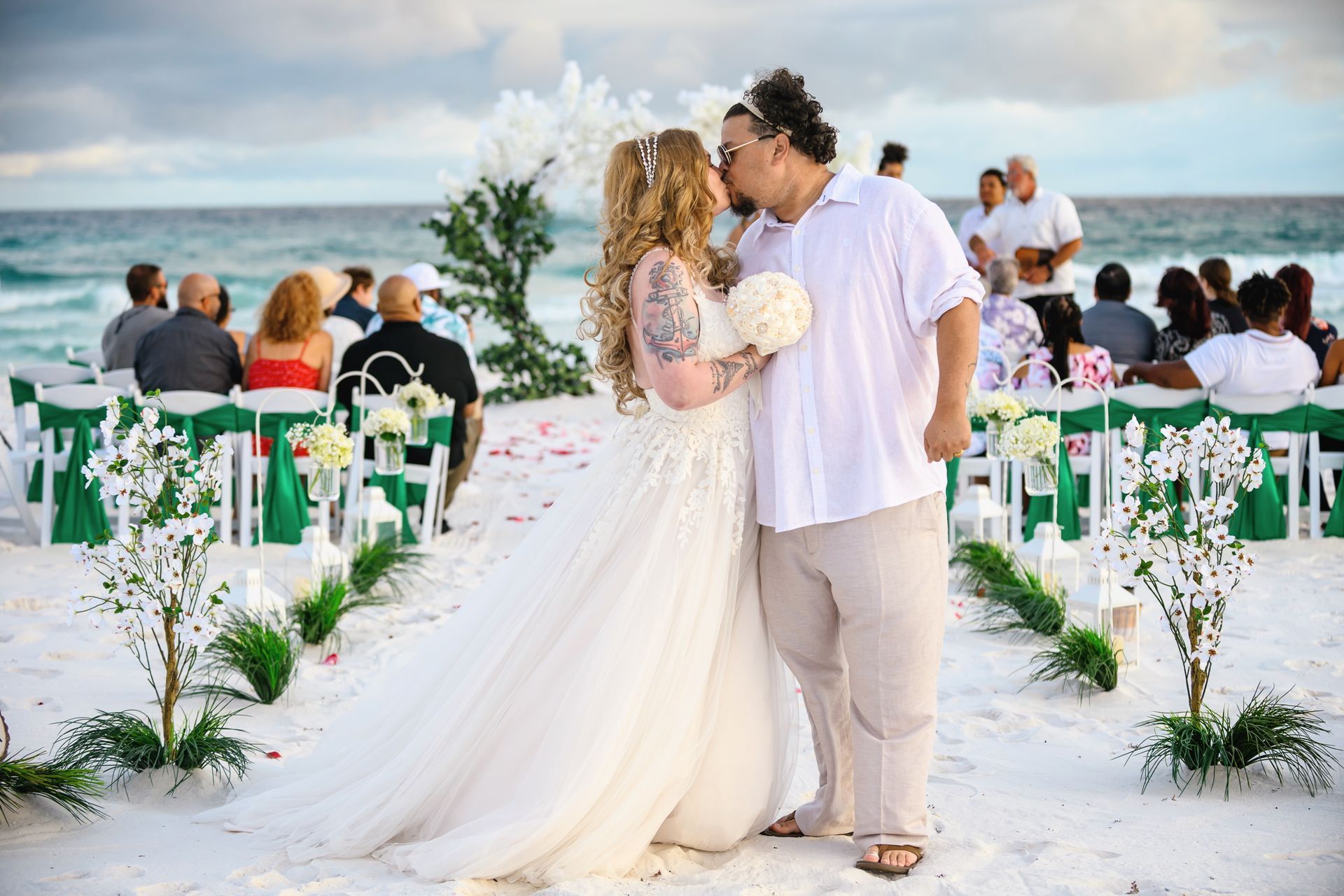 Couple kissing at a beach wedding aisle with white chairs and floral arrangements