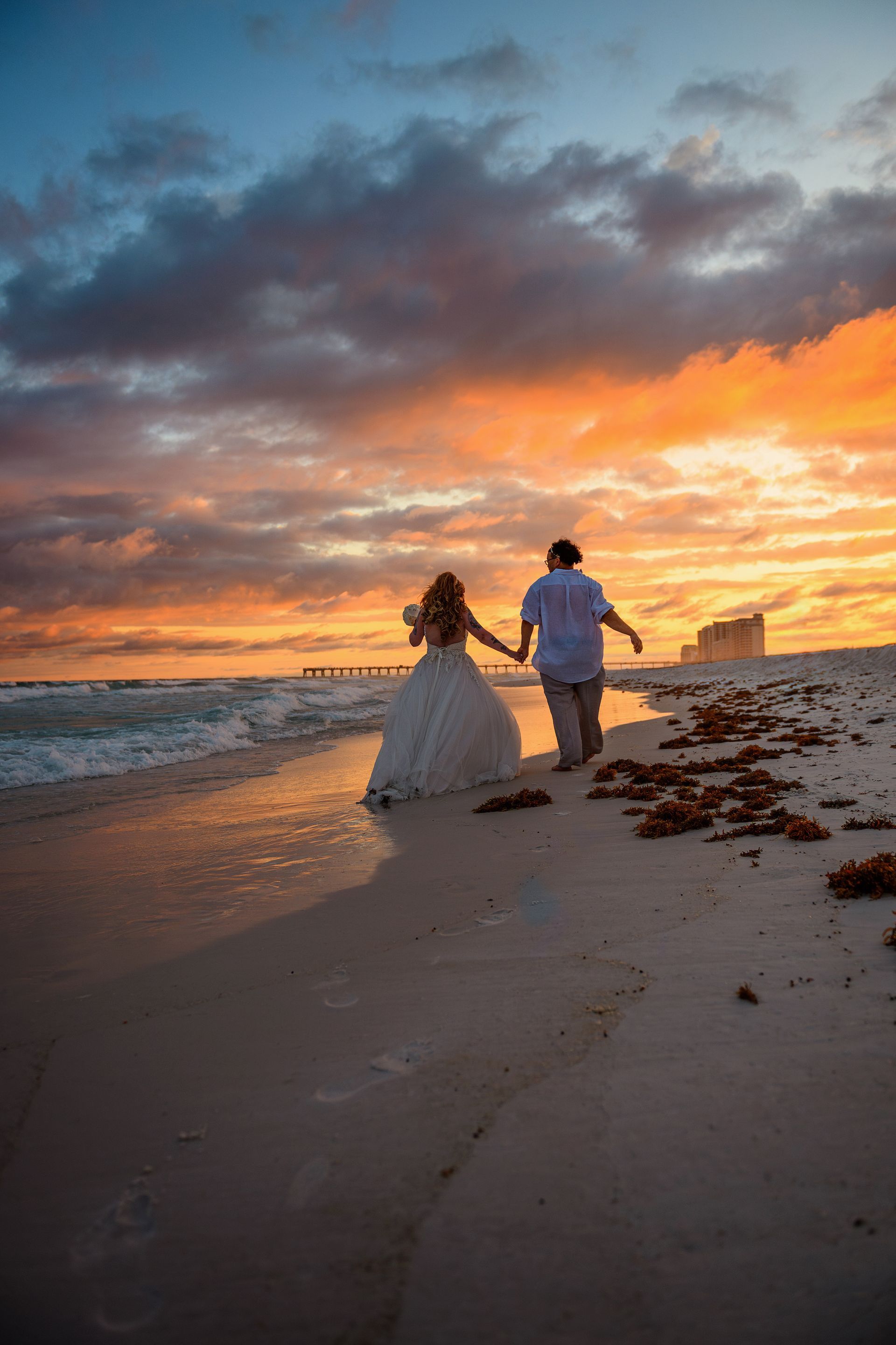 bride and groom holding hands and walking on beach at sunset