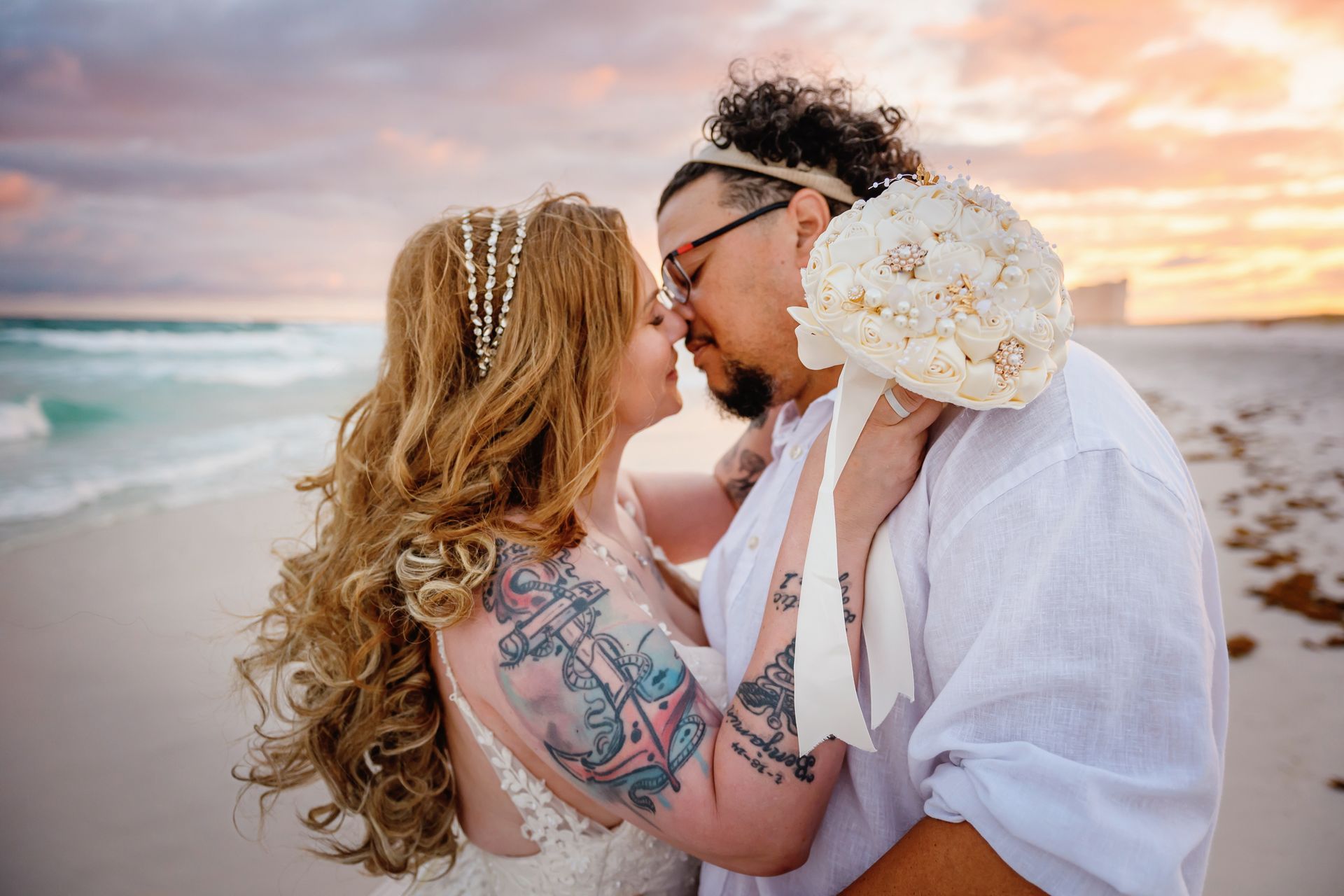 Couple embracing on a beach at sunset, with the ocean and pastel sky behind them
